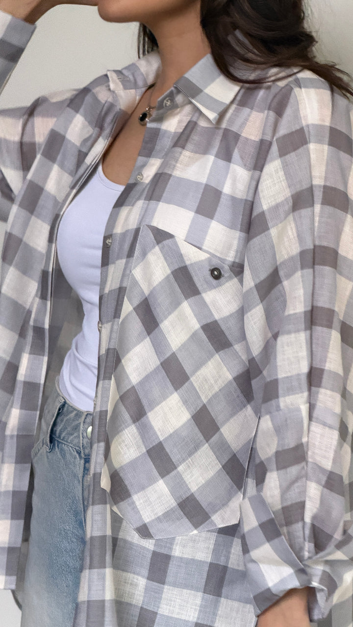 A woman wearing a gray and white plaid button-up shirt over a white tank top and light blue jeans.