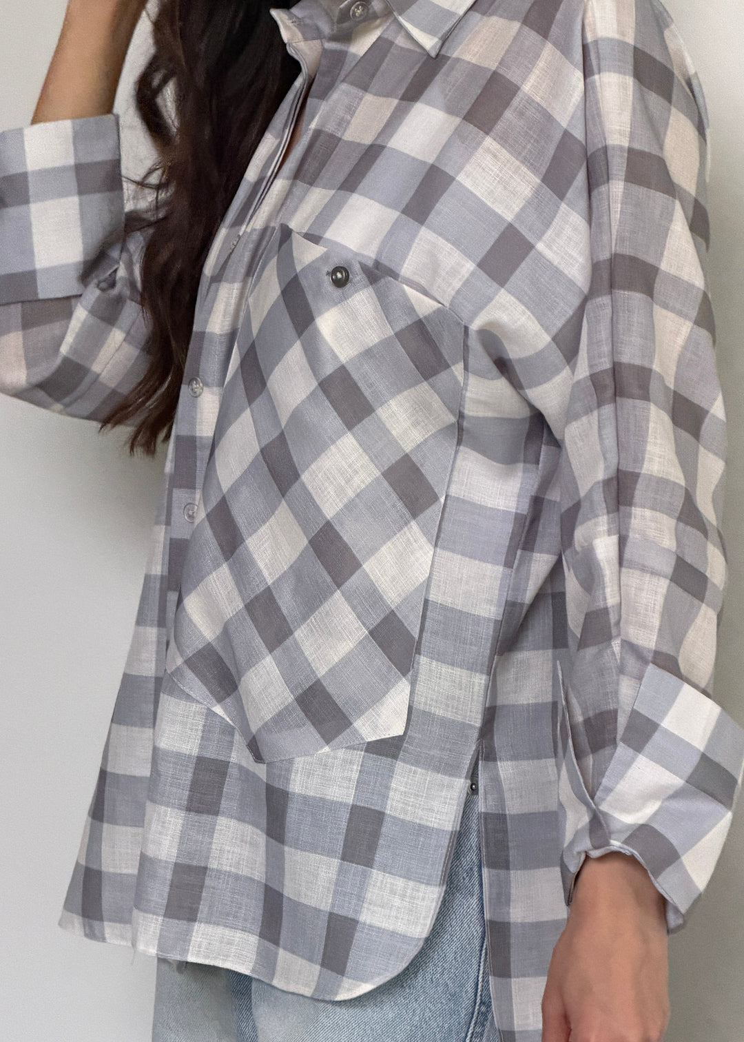 A woman wearing a gray and white plaid button-down shirt with a chest pocket, paired with light-wash jeans, shown in a close-up lifestyle shot.