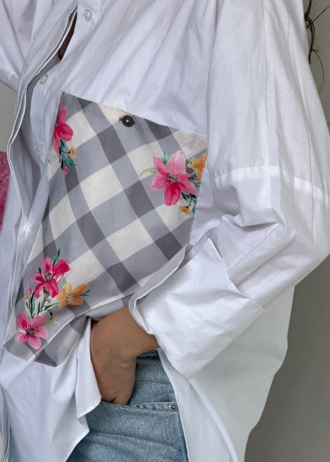 A close-up of a person wearing an oversized white button-up shirt and light blue jeans, holding a gray-and-white gingham pocket square with pink and orange floral print.