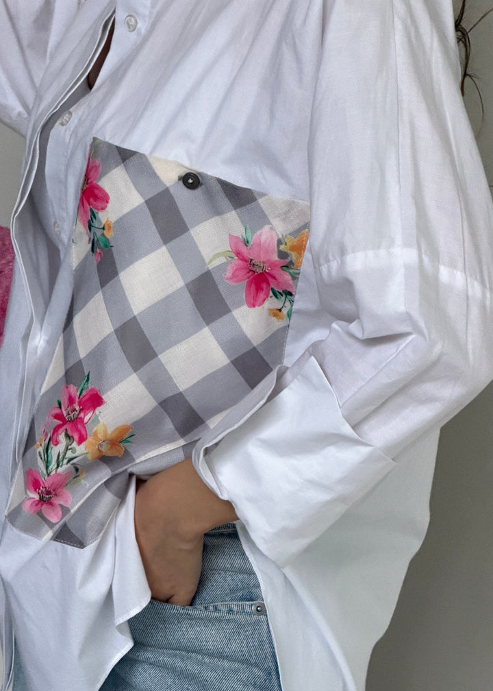 A close-up of a person wearing an oversized white button-up shirt and light blue jeans, holding a gray-and-white gingham pocket square with pink and orange floral print.