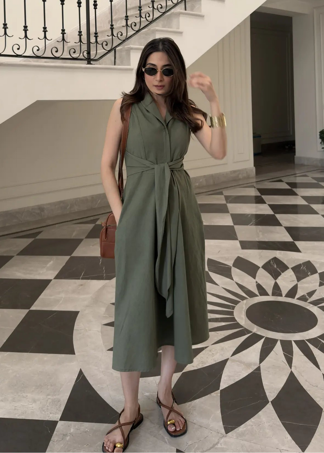 Woman in a green dress posing in a elegant interior setting with staircase and checkered floor.