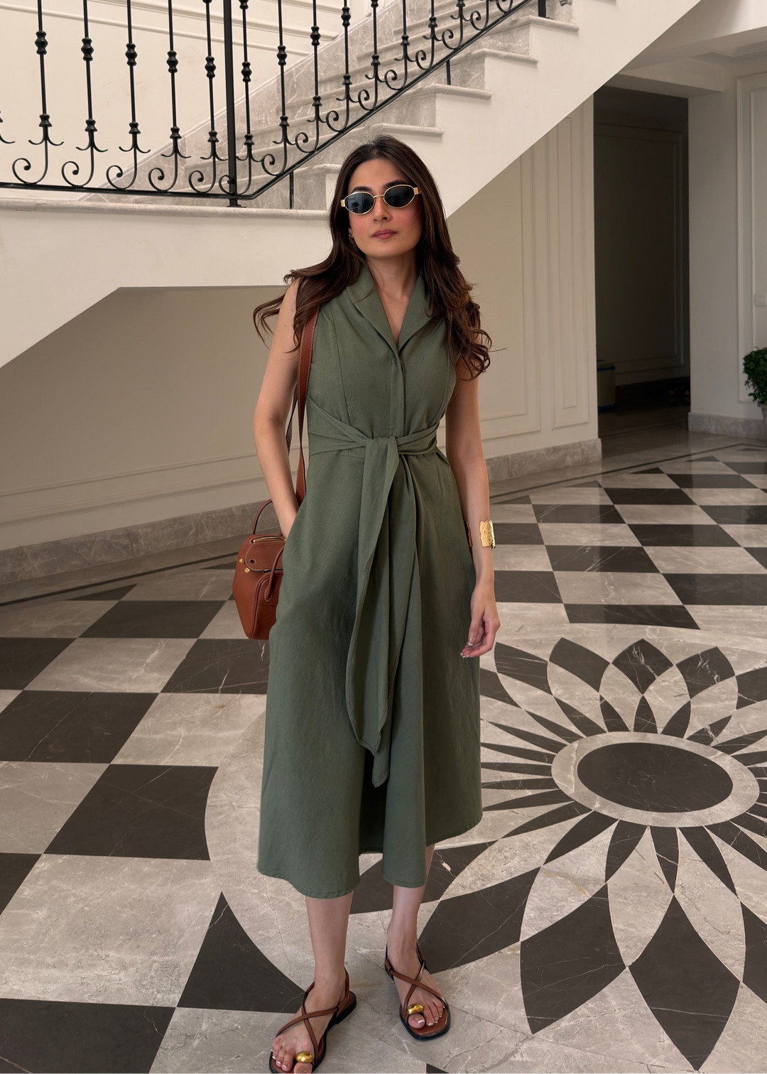 Woman in a green dress standing on a checkered floor with a staircase in the background