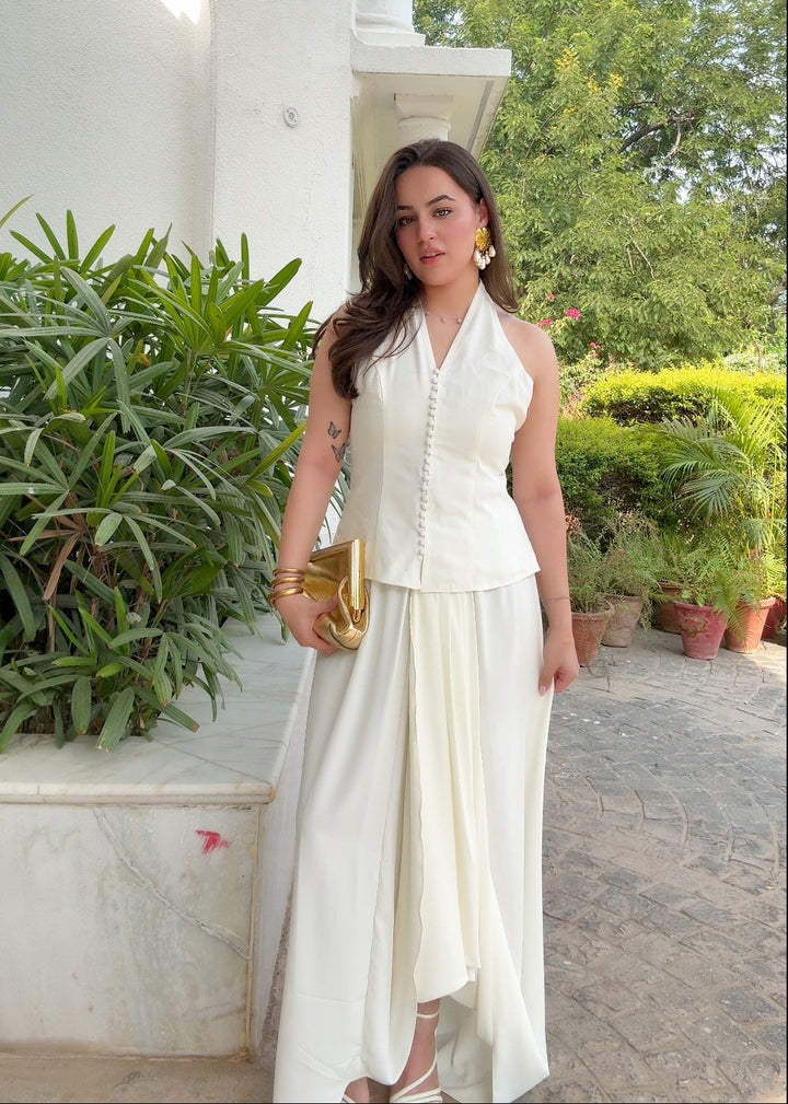 Woman in a white outfit standing outdoors with greenery in the background