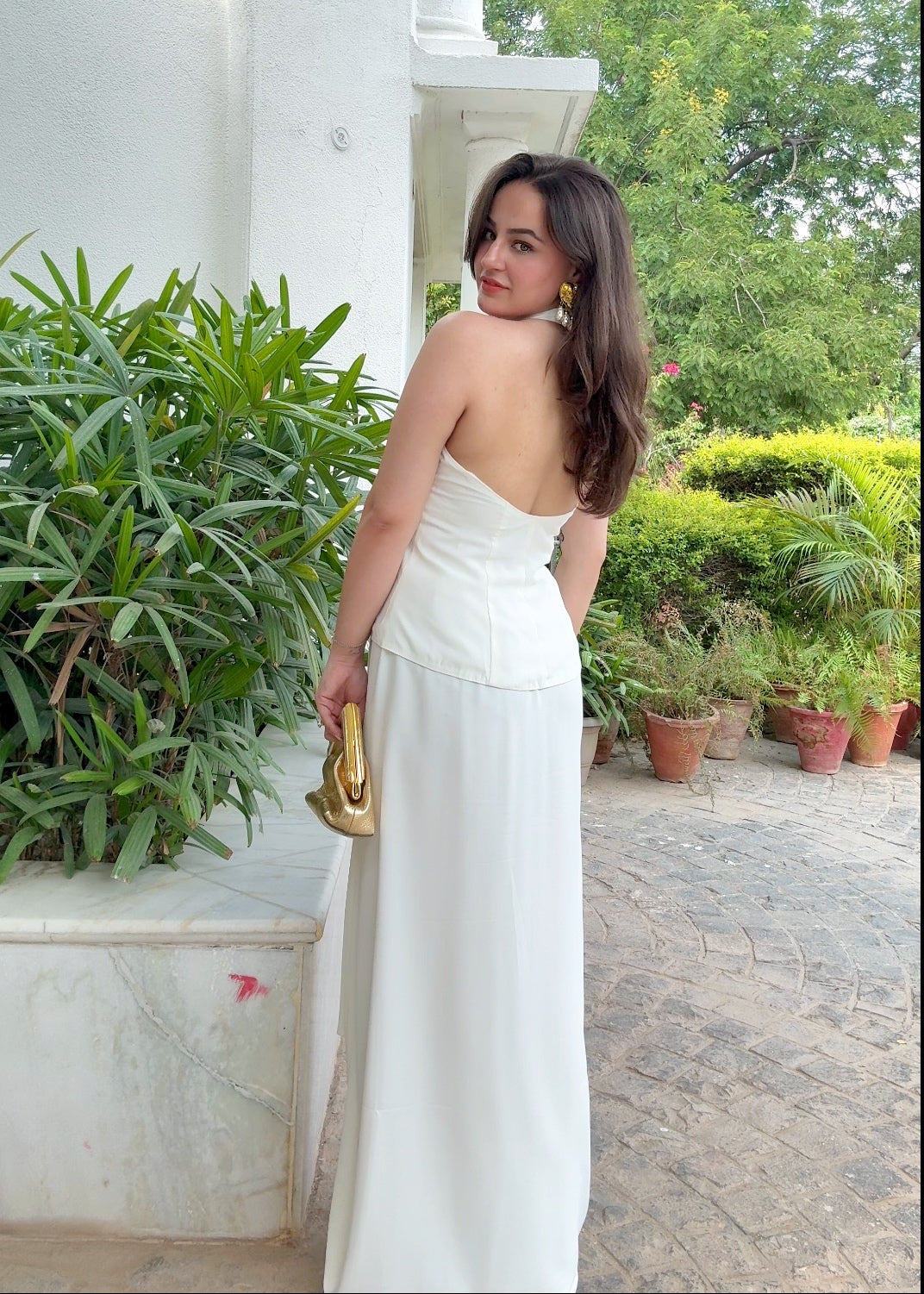 Woman in a white dress standing outdoors with greenery and a building in the background