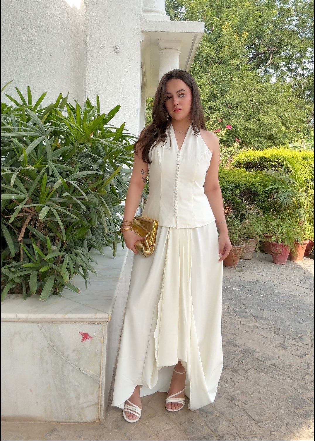 Woman in a white outfit standing outdoors with greenery in the background
