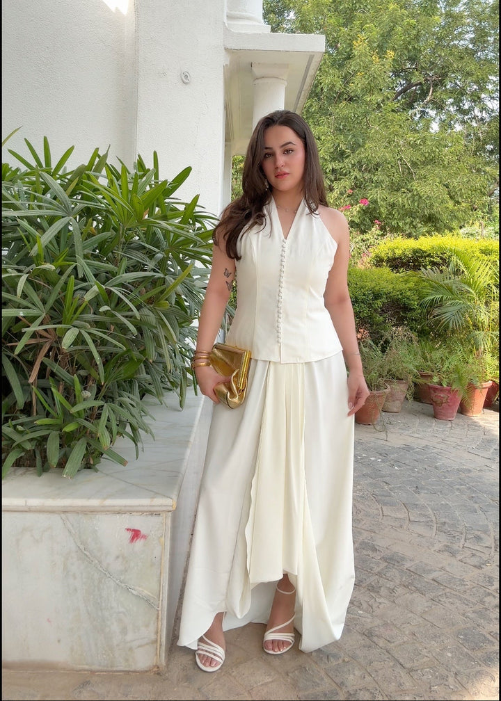 Woman in a white outfit standing outdoors with greenery in the background