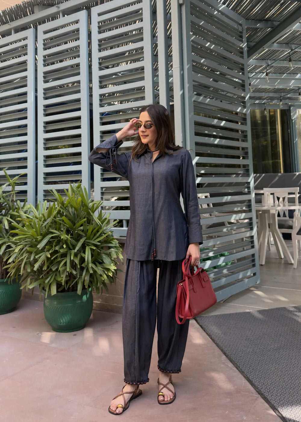 Woman in a gray outfit with a red bag standing in front of a modern architectural structure.