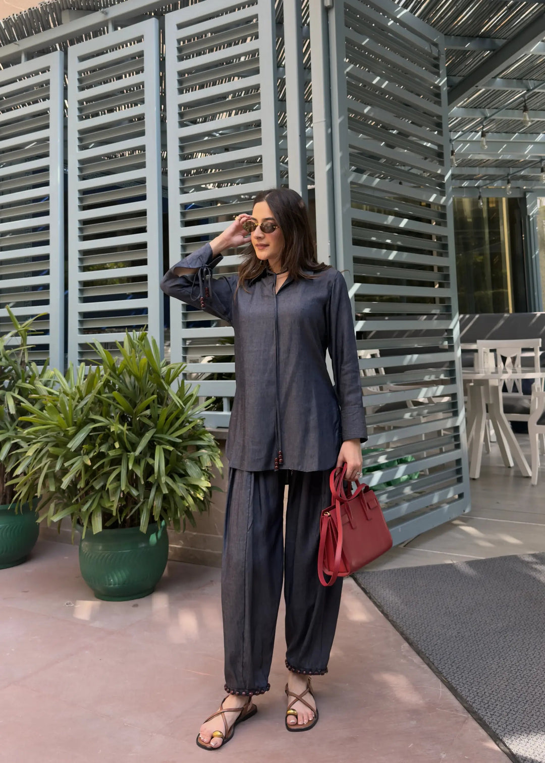 Woman in a gray outfit with a red bag standing in front of a modern architectural structure.