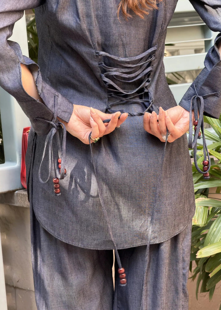 Person wearing a dark gray outfit with fringe details, sitting outdoors.